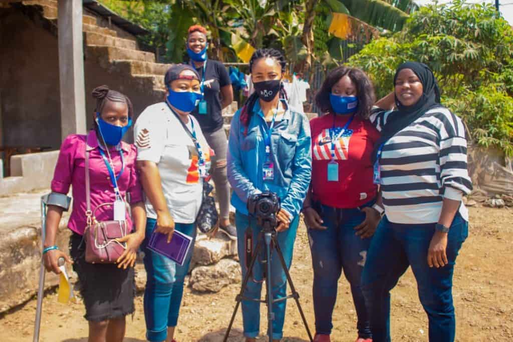 5 women stand behind a camera and tripod