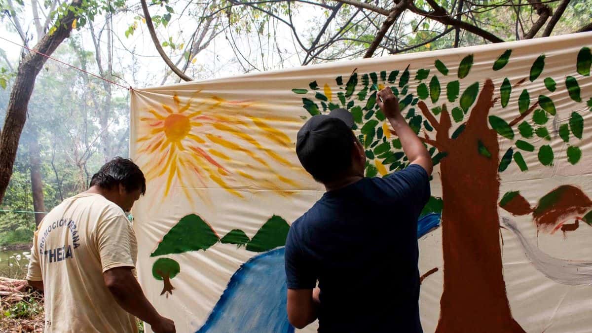 Two men paint a landscape scene on an outdoors canvas