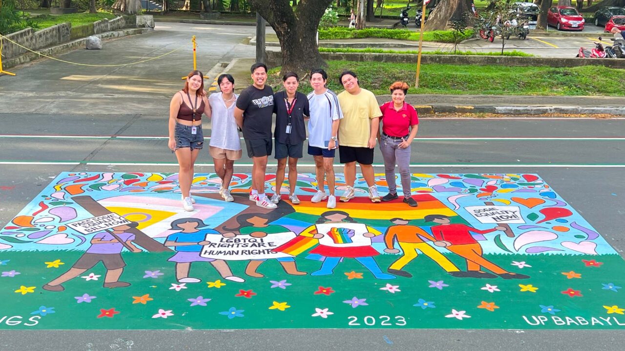 LGBTQ+ rights activists standing on a mural about the SOGIE Equality Bill in the Philippines