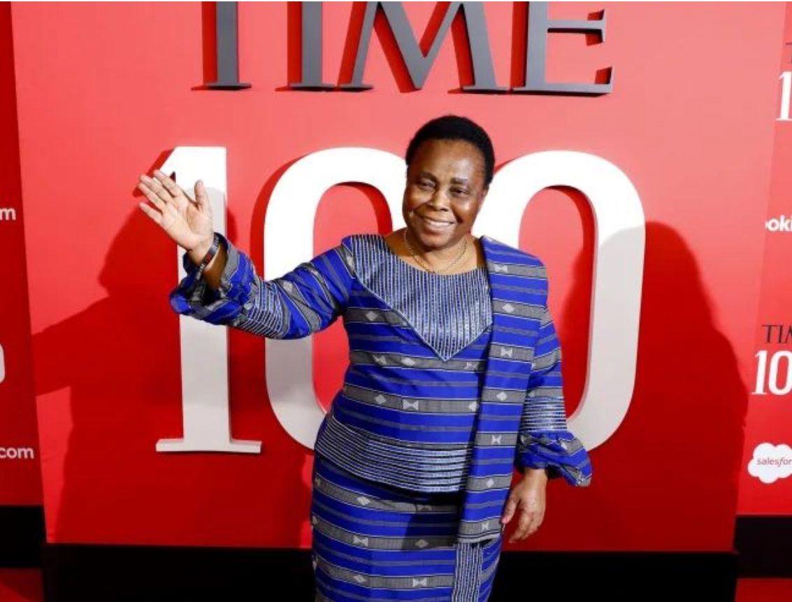 Julienne_SOFEPADI Julienne, an African woman with cropped hair, waves as she walks the Time100 red carpet in a violet dress